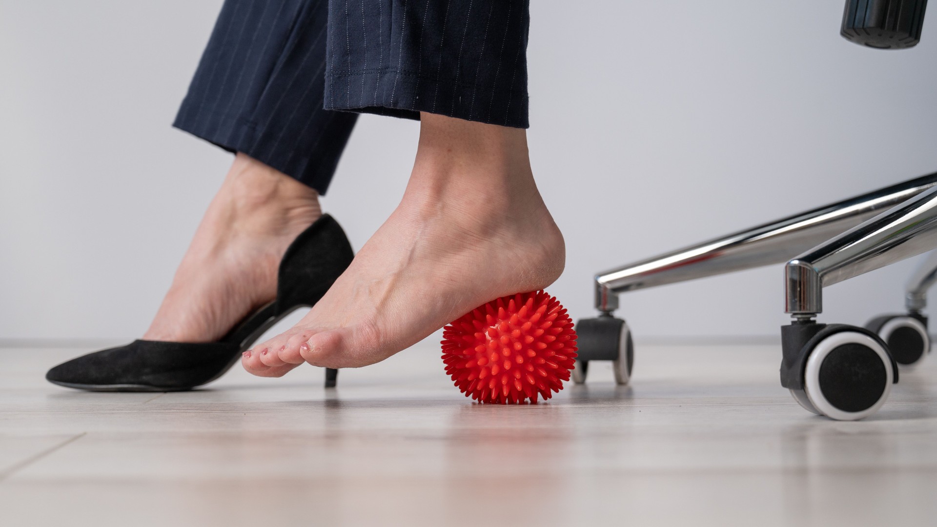 Business woman massages her feet on a massage ball with spikes.